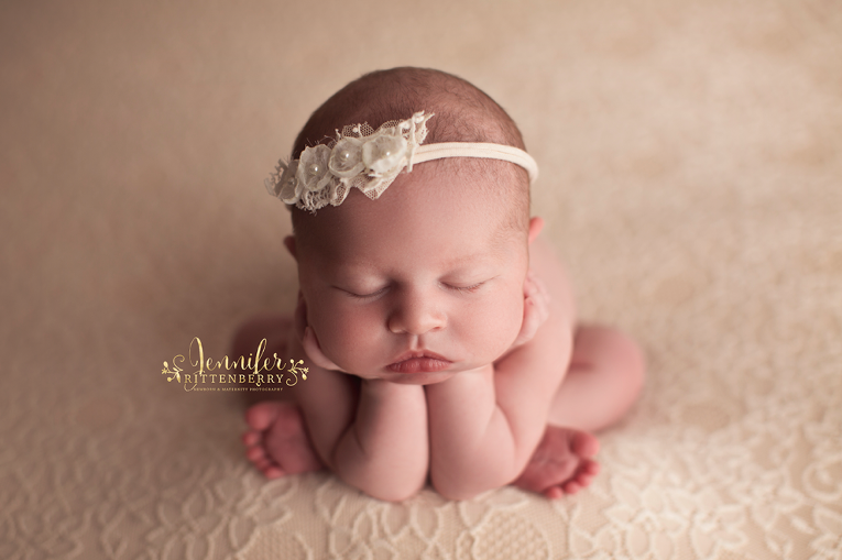 newborn infant in froggy pose on light peach fabric