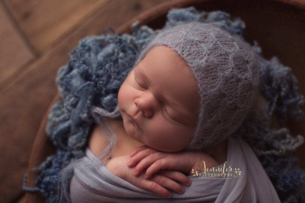 newborn infant wrapped and posed in a wooden bowl dressed in shades of blue