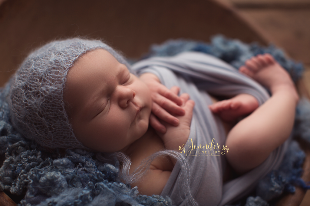 newborn infant wrapped and posed in a wooden bowl dressed in shades of blue